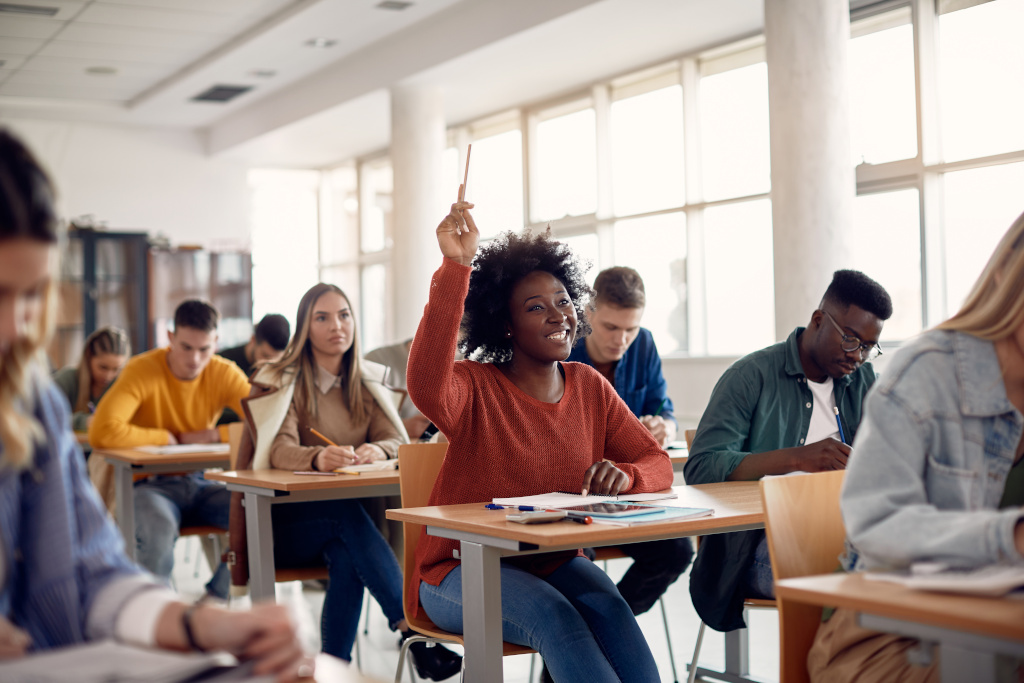 happy black student raising arm to answer question while attending class with her university colleagues.